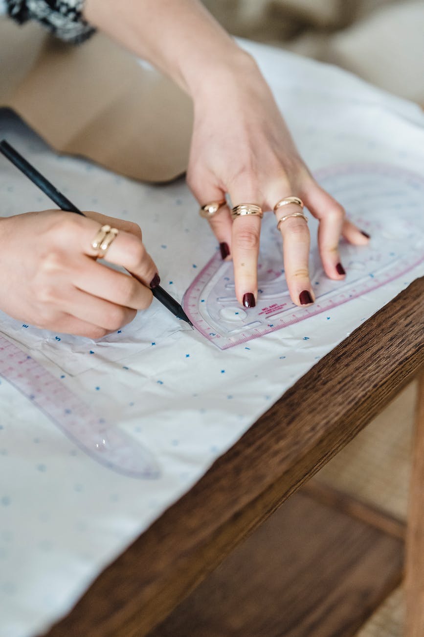 crop seamstress tracing on paper with sewing ruler in workshop