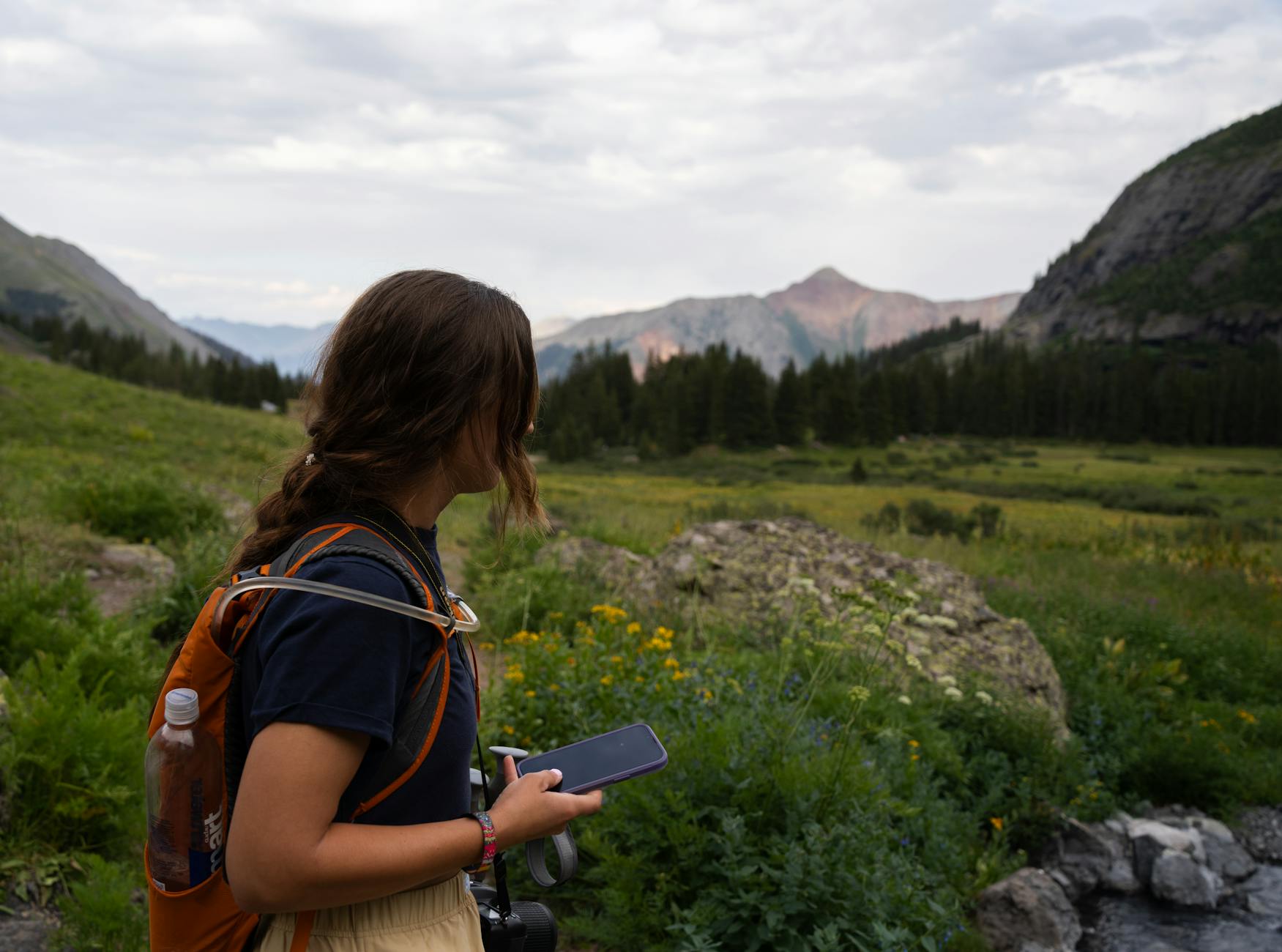 a woman with a backpack looking at a cell phone ready to camp