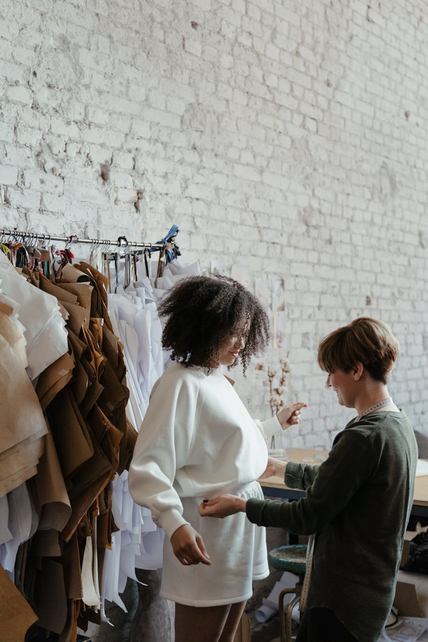 photo of woman wearing white sweater while fashion designer adjusts it
