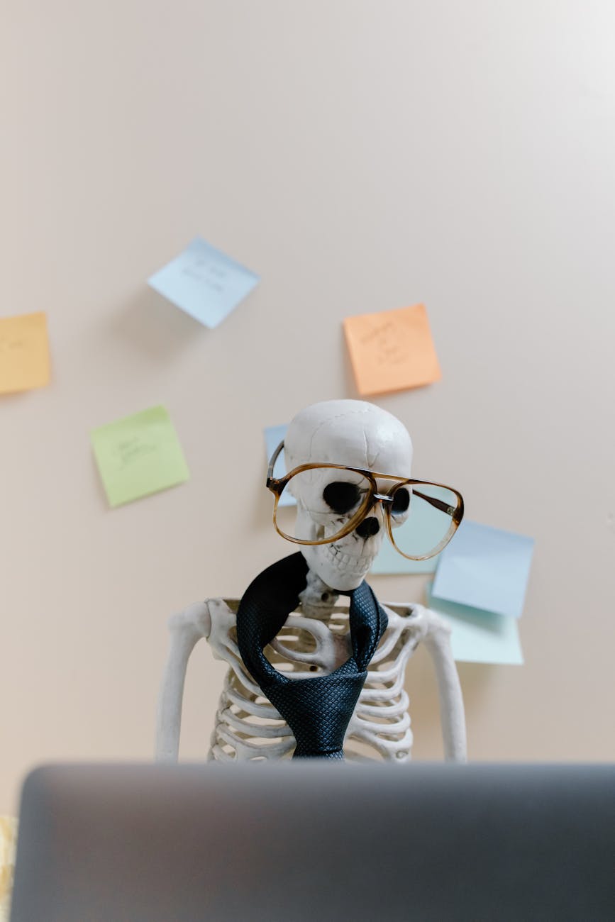 burned out skeleton wearing brown glasses working at their computer
